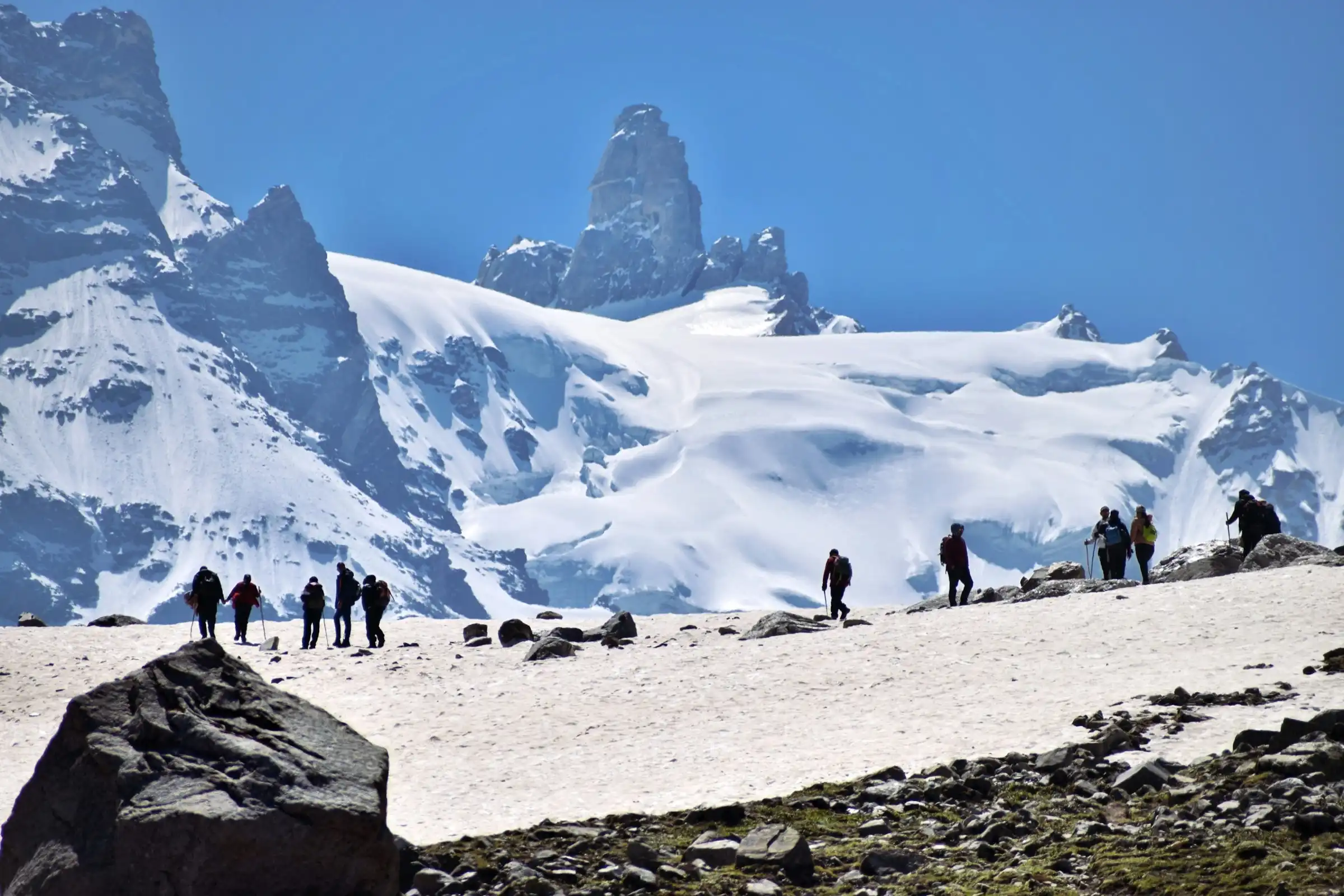 A line of trekkers crossing a snowfield below a rock tower on the Hampta Pass trek