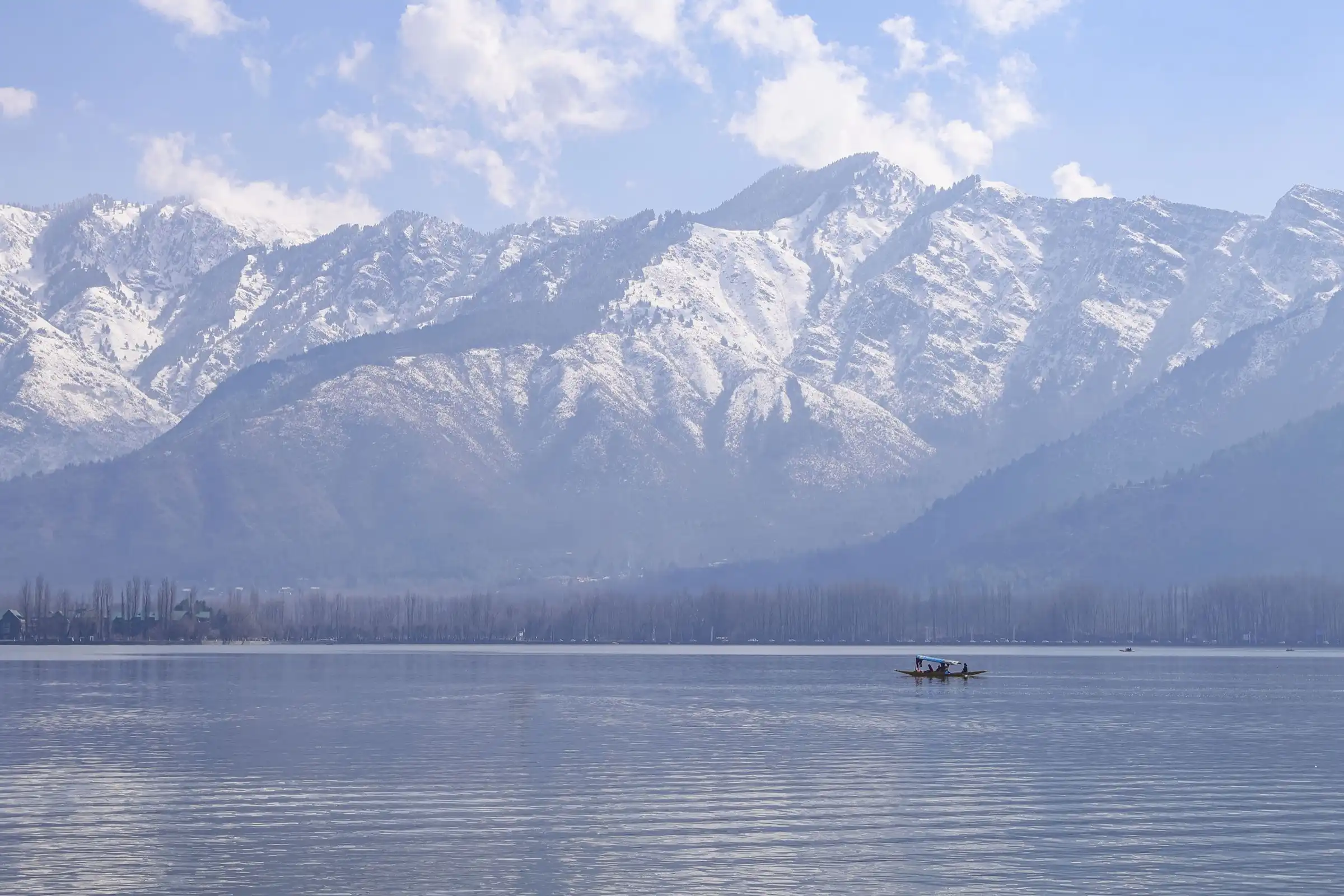 A lone shikara crossing Dal Lake below a wall of snow-covered mountains