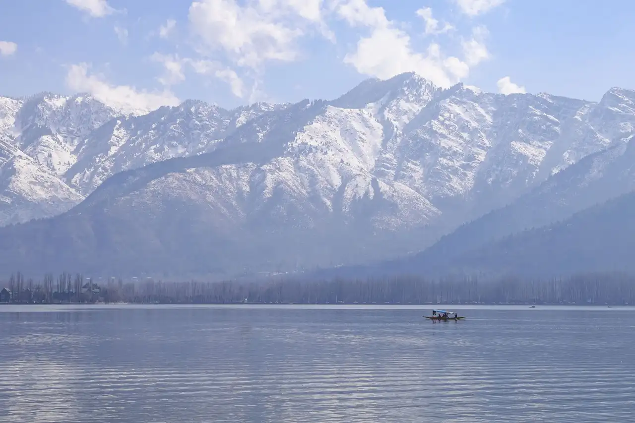 A lone shikara crossing Dal Lake below a wall of snow-covered mountains
