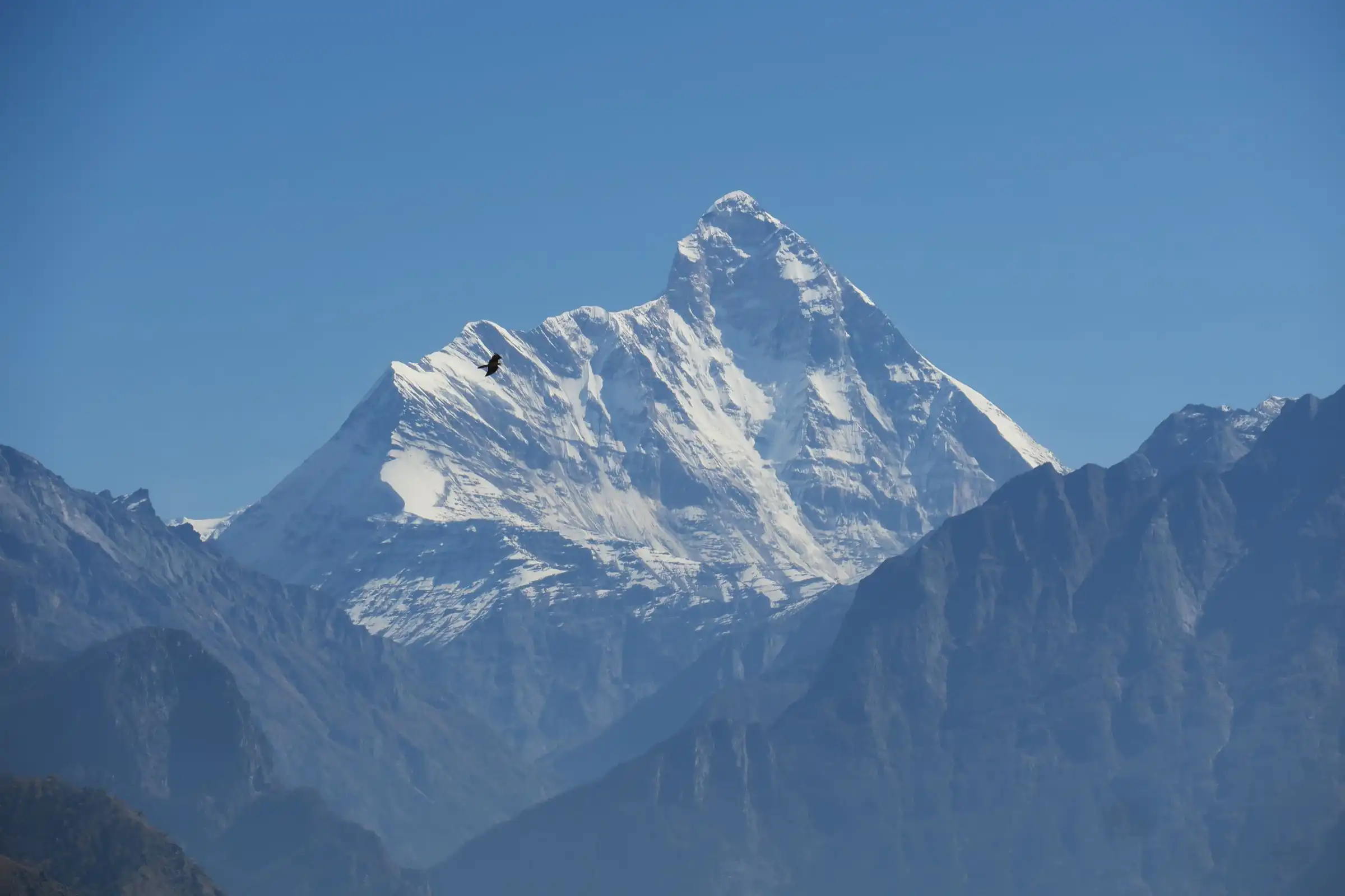 The pyramid summit of Nanda Devi above hazy blue ridges, seen from Auli