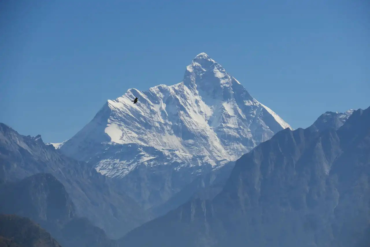 The pyramid summit of Nanda Devi above hazy blue ridges, seen from Auli